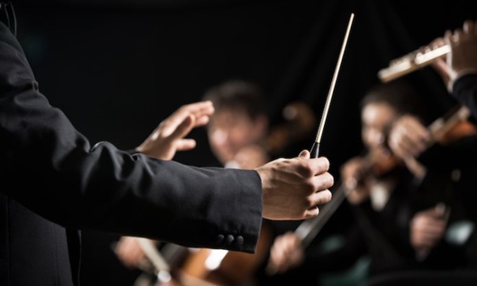 Orkestra Şefi Kimdir? Orkestra Şefi Ne Kadar Kazanır? Müziğin büyülü dünyasında izleyiciyi derinden etkileyen performansların arkasında çoğu zaman görünmeyen bir lider vardır: orkestra şefi. Sahnenin önünde, elindeki baton ile onlarca müzisyeni yöneten bu kişi, yalnızca ritim tutan biri değil, aynı zamanda müziğin ruhunu şekillendiren bir sanatçıdır. Klasik müzikten film müziklerine kadar geniş bir alanda görev alan orkestra şefi, sanat ve disiplinin birleştiği özel bir mesleği temsil eder. Konulu bir haber görseli.